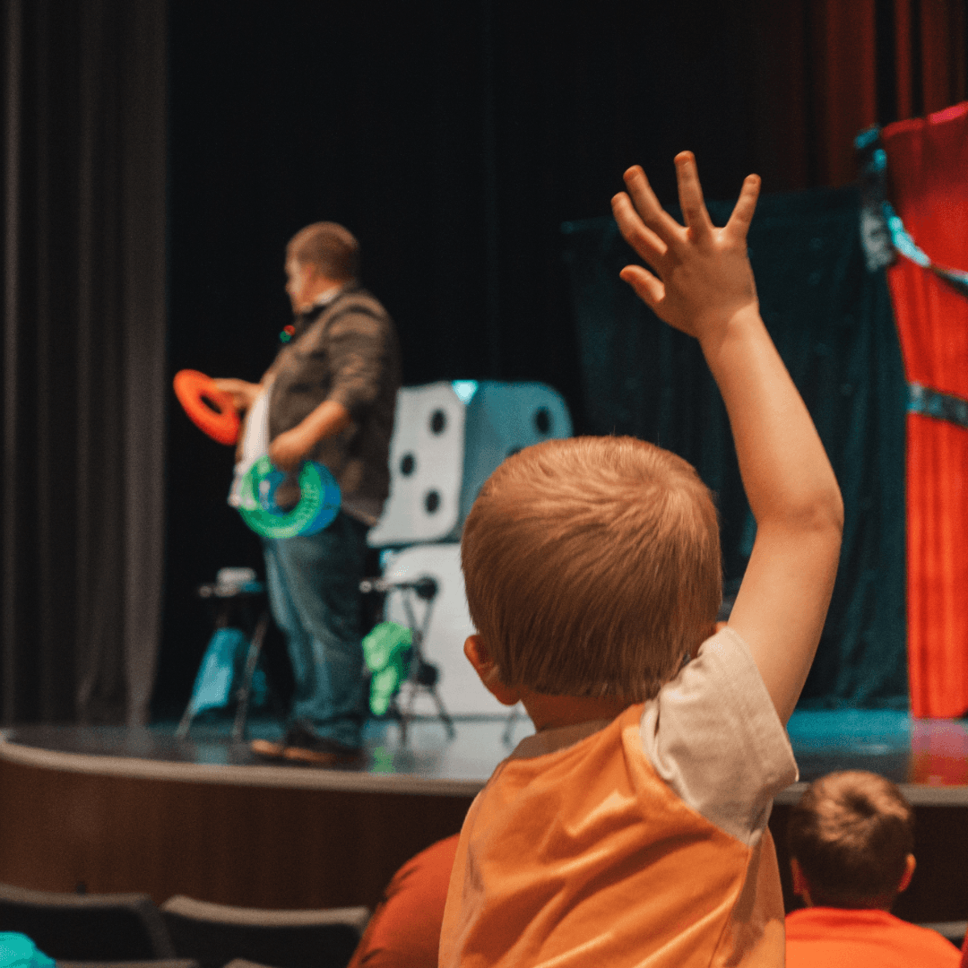 guy on stage performing magic and a kid in the crowd watching